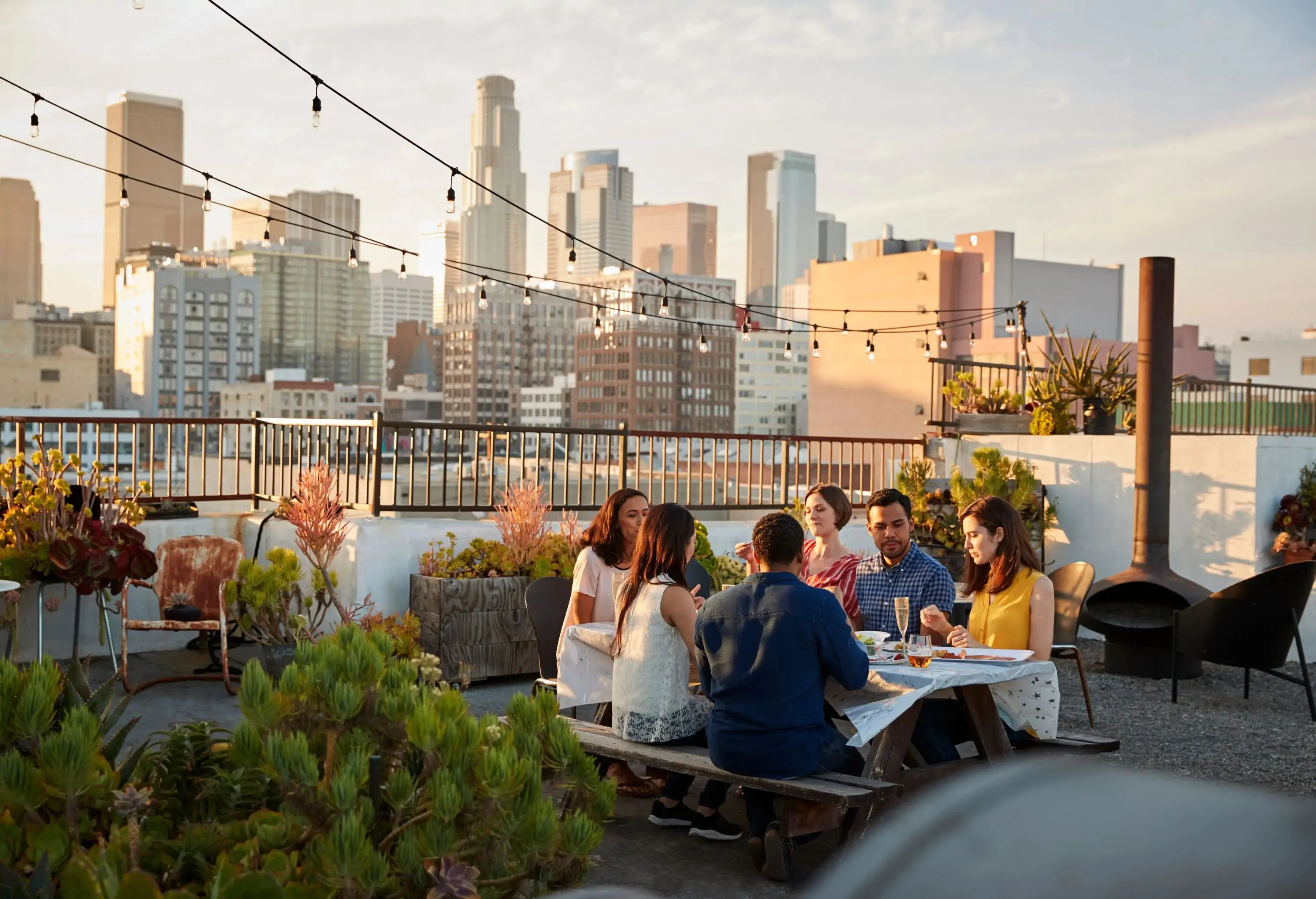 Friends Gathered On Rooftop Terrace For Meal With City Skyline In Background