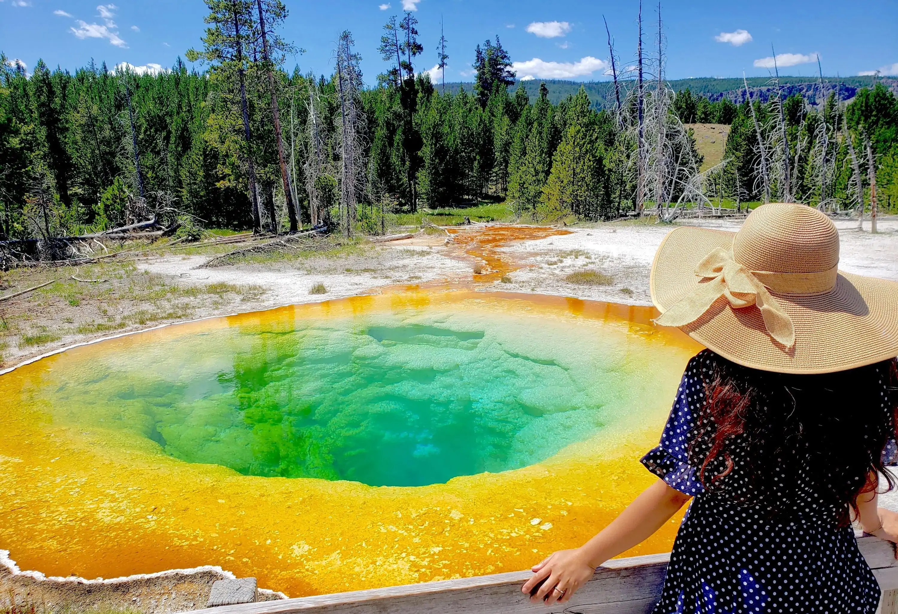 A woman in a beach hat looking at a unique hot spring with a bright yellow rim.