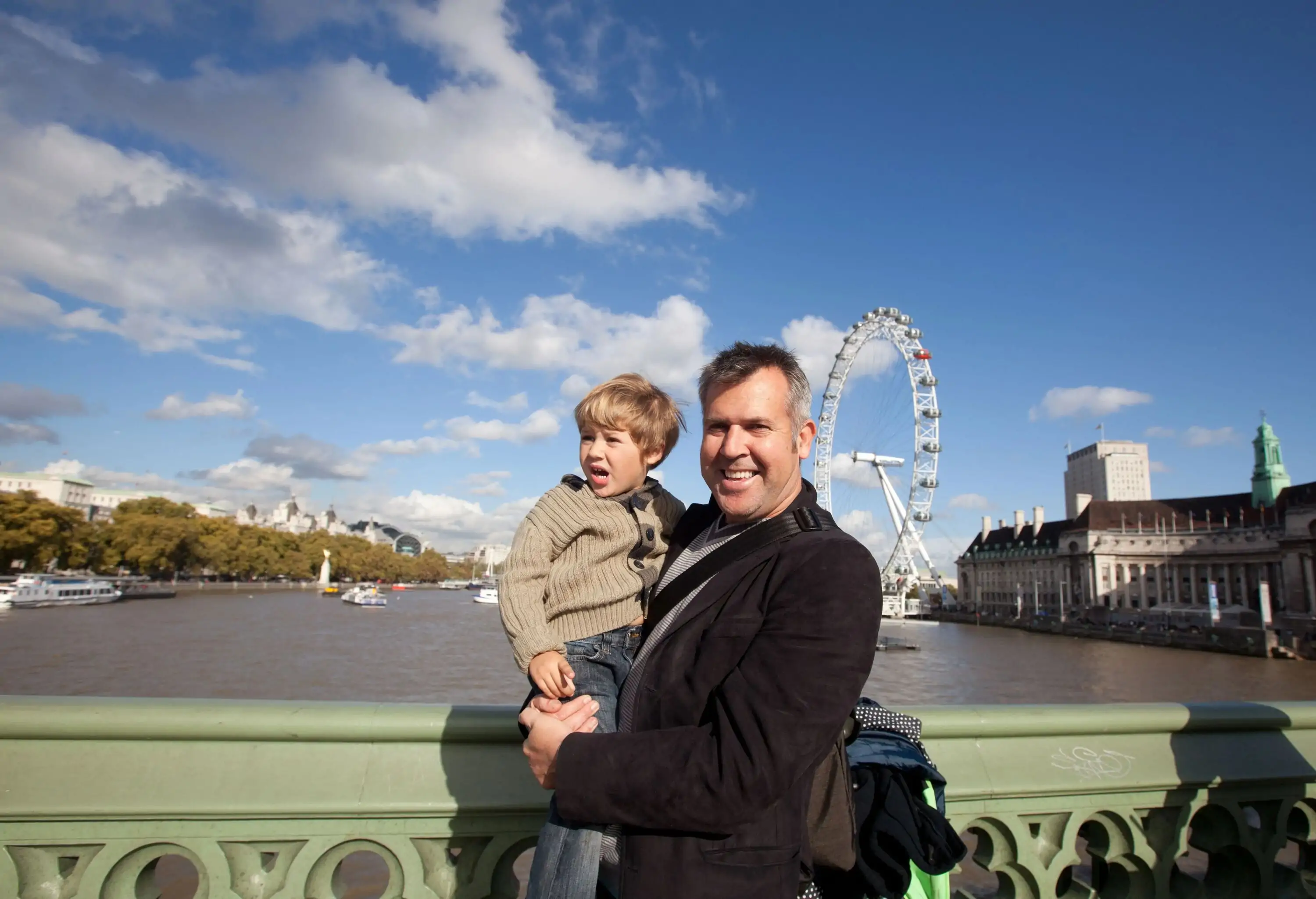 Father and son stand on Westminster bridge with London eye in background.