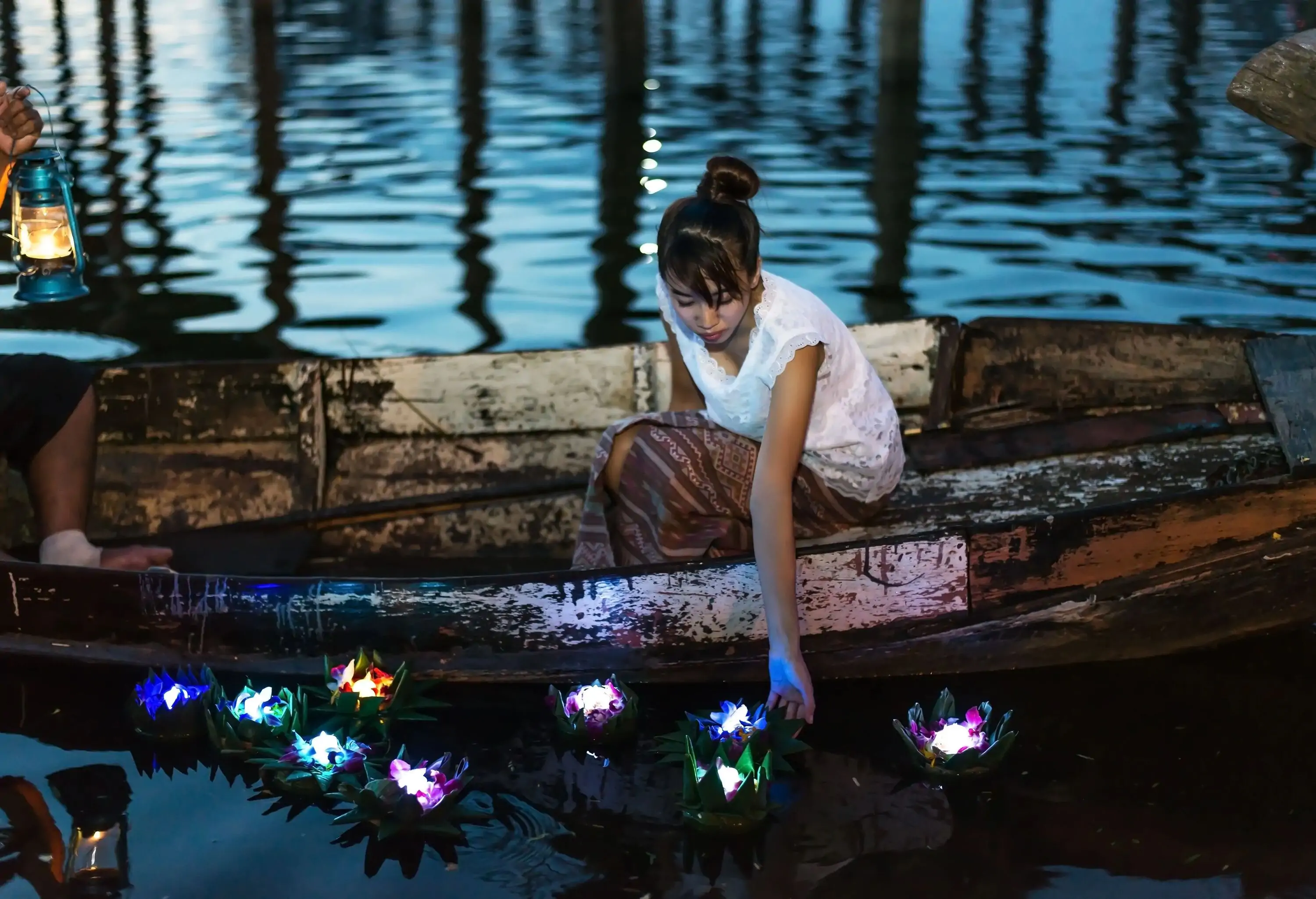 Woman sitting a small wooden boat lighting floating lanterns