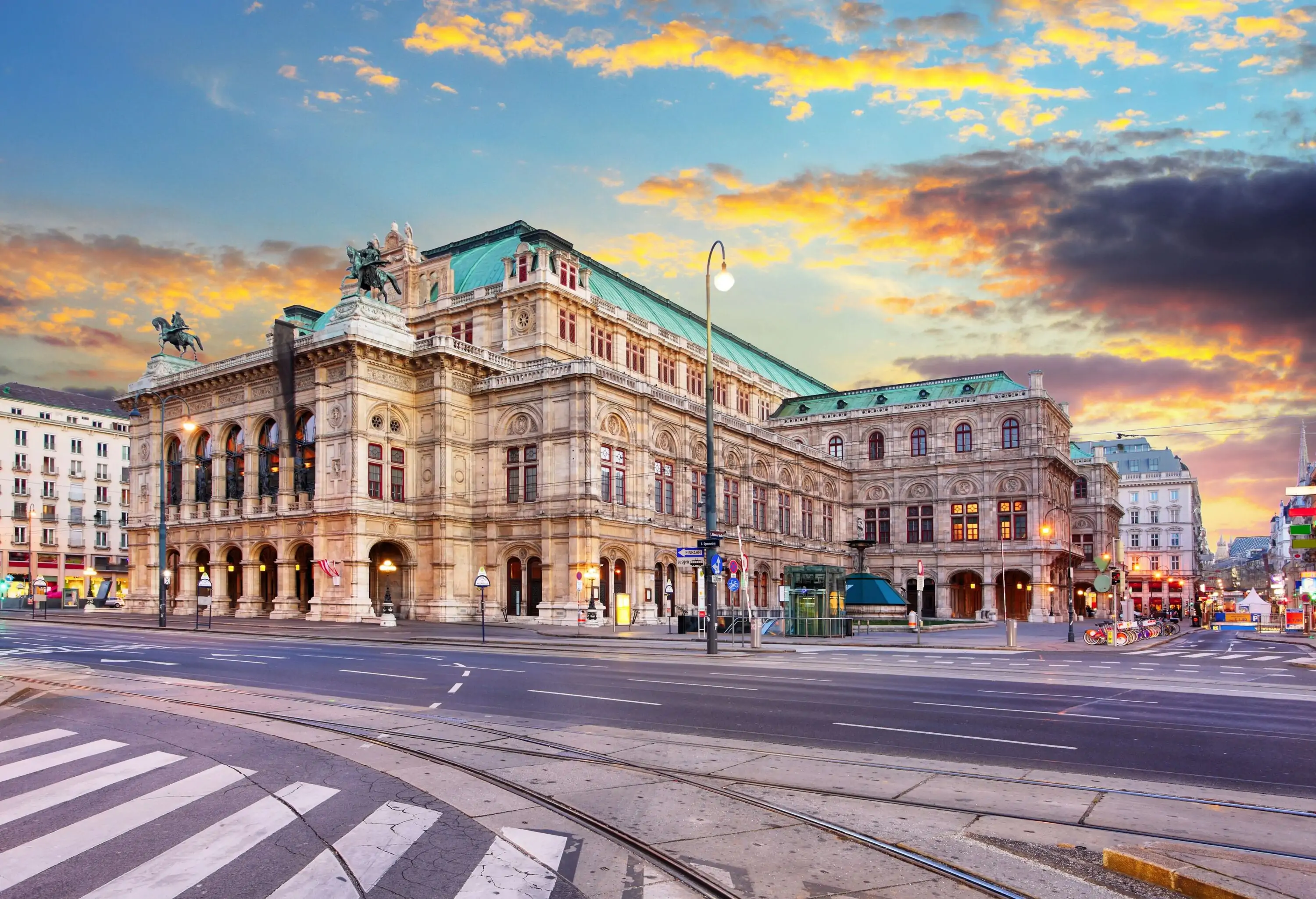 The grandiose Schönbrunn Palace, displaying ornate Baroque architecture with its imposing yellow facade, tall windows, and elaborate rooftop statues, stands majestically at the backdrop of its beautifully manicured Great Parterre garden, dotted with leisurely strolling visitors.