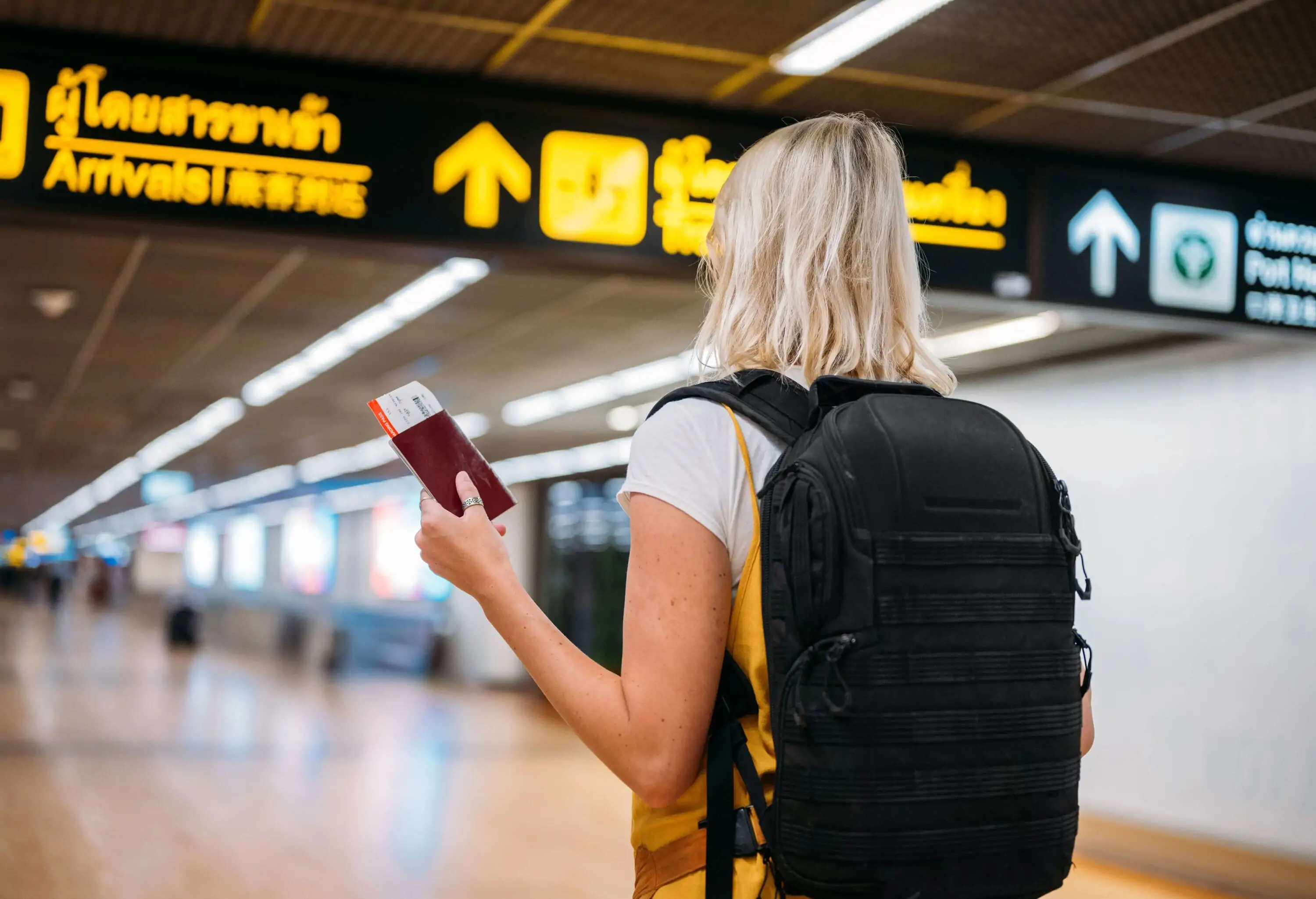 Rear view of a woman at the airport holding a passport with a boarding pass.